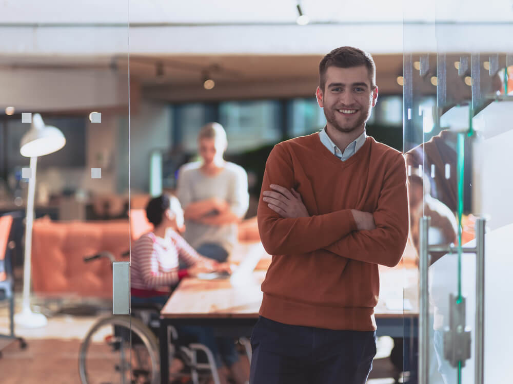 Handsome casual businessman standing confident in the office. Disabled businesswoman in wheelchair working together with the team in the background